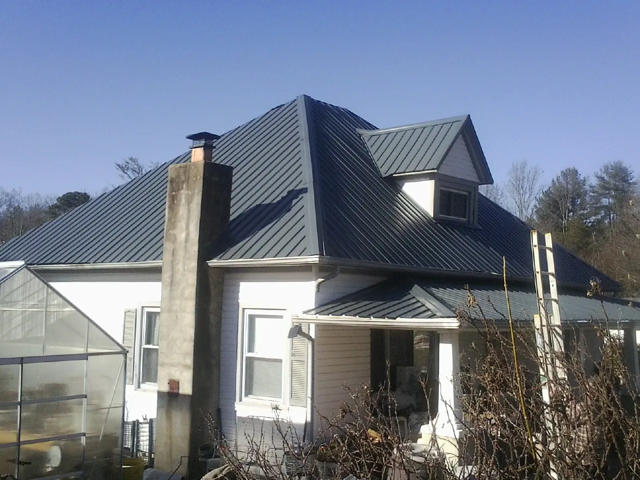 Dark blue standing seam metal roof on a white farmhouse with dormer — Slate & Tile Roof Repair by Roofing Brothers in Seibert