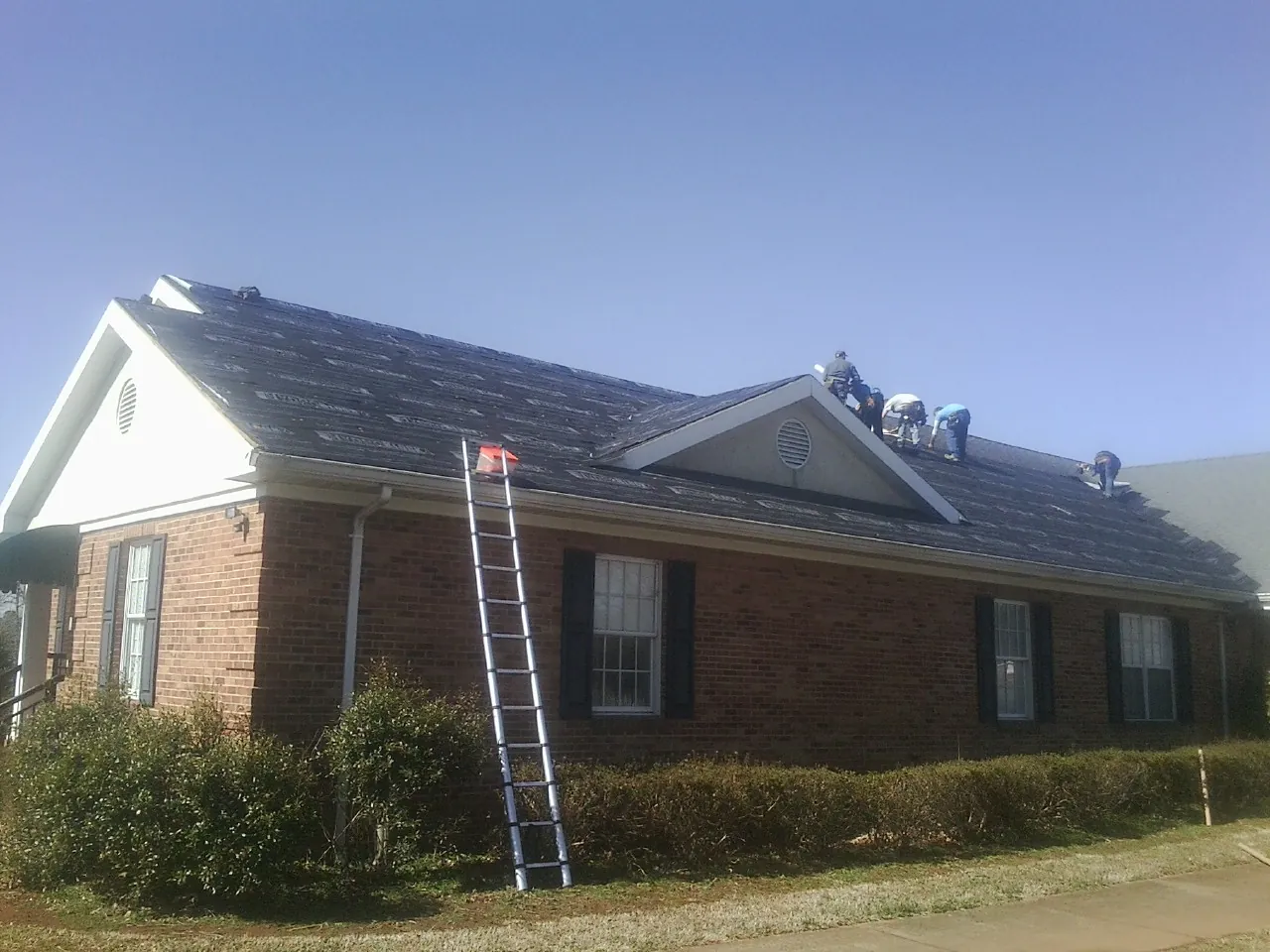 Crew tearing shingles off a brick ranch roof with a ladder set — Emergency Roof Repair work by our crew in Seibert