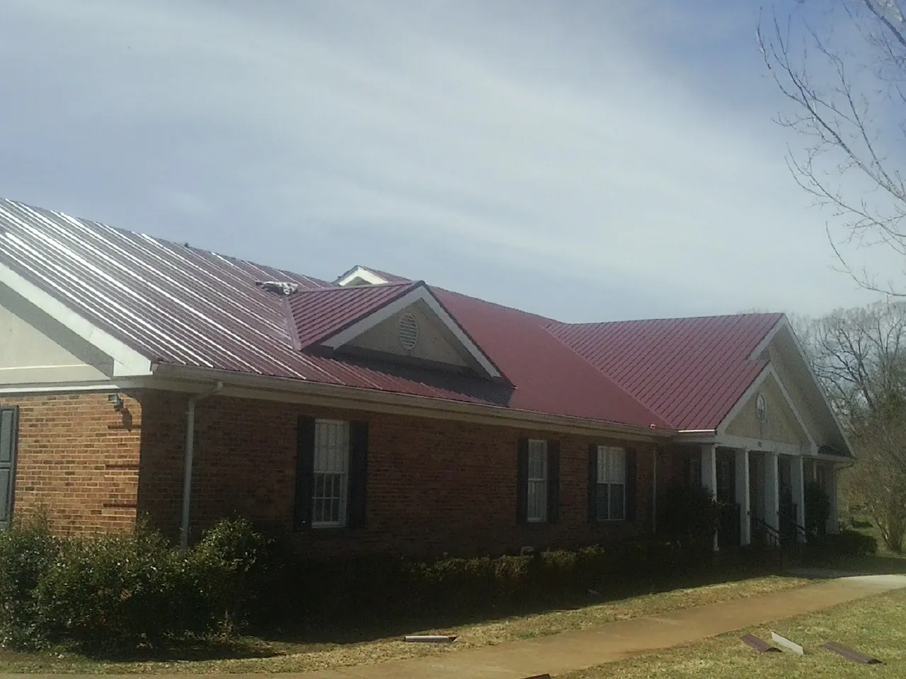 Red metal roof with gabled entries on a long brick building, from a Hail Damage Roof Repair job in Seibert