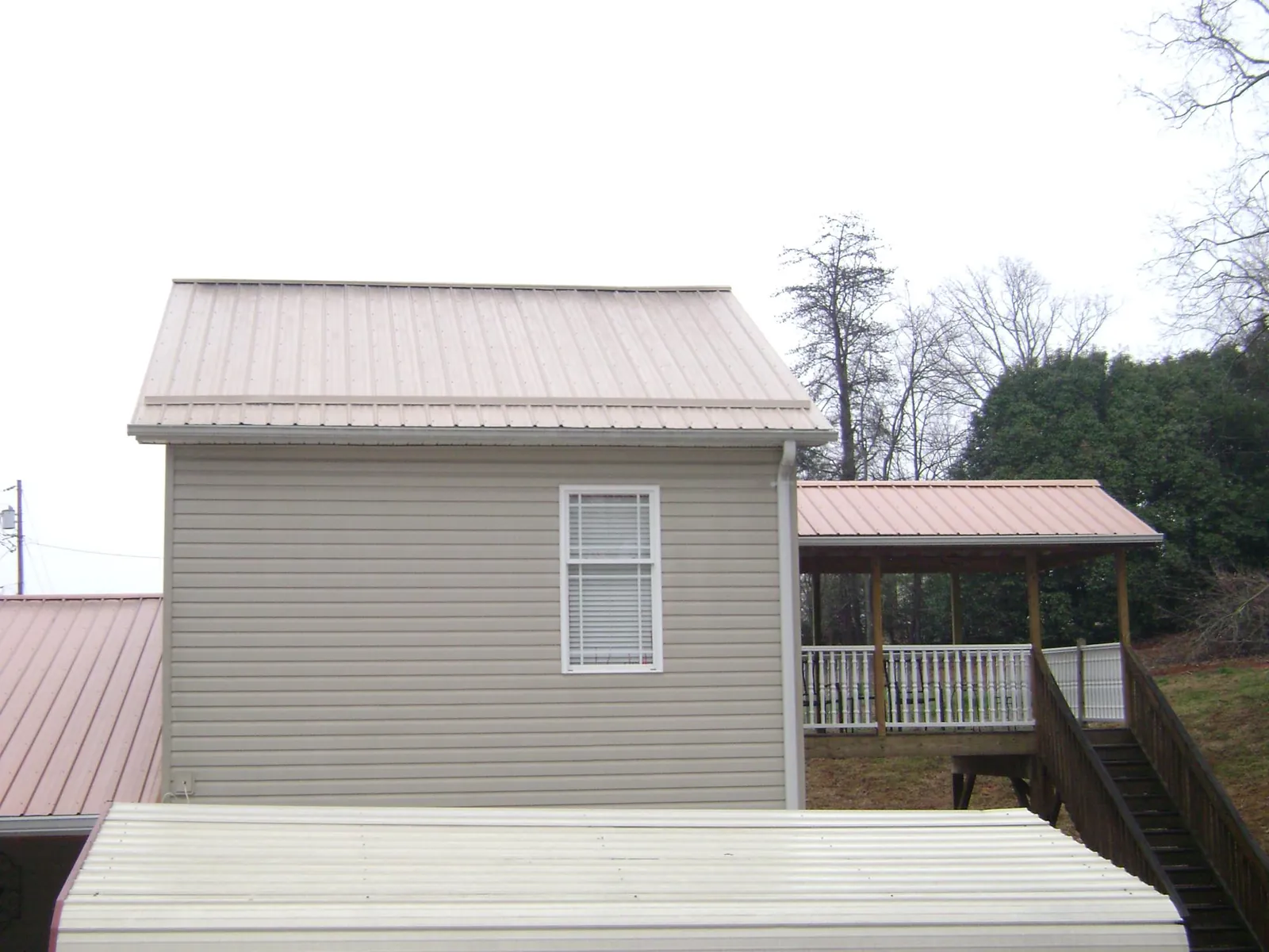 Tan metal roofs on a two story addition and attached porch, from a Roof Replacement job in Seibert
